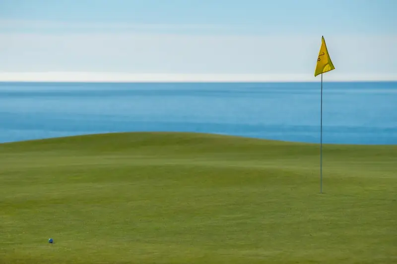 Un drapeau jaune sur un green, au bord de la mer